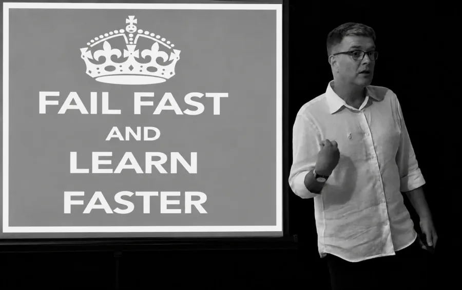 Nir Tsuk speaking beside a slide reading “Fail fast and learn faster”
