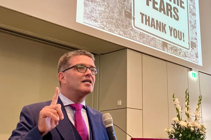 A conference hall: Nir Tsuk at a lectern with a microphone, under a slide reading “Please do not feed the fears”.