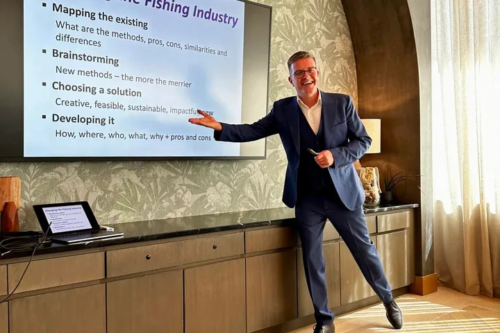 Nir Tsuk smiling and pointing to a large screen with a slide titled “Changing the Fishing Industry”.