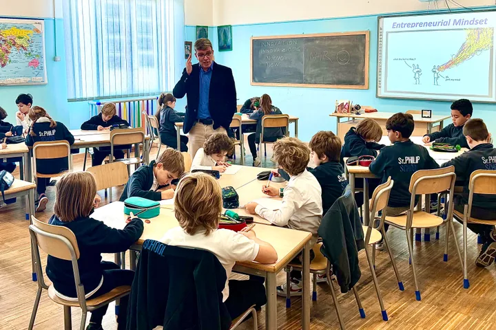 A primary-school classroom: children in uniform working at desks, Nir Tsuk standing among them, “Entrepreneurial Mindset” on the board.